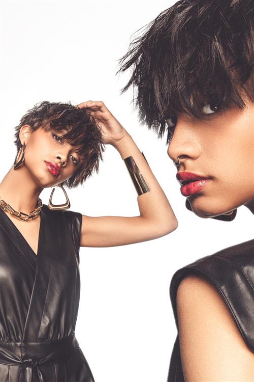 Woman with shaggy haircut wearing black outfit with gold accessories.